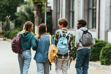 Fyra ungdomar med ryggsäckar går bredvid varandra i skolmiljö med ryggarna mot kameran