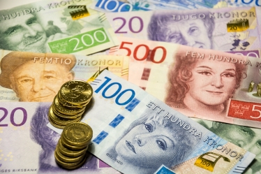 Närbild på svenska sedlar och mynt som ligger huller om buller.