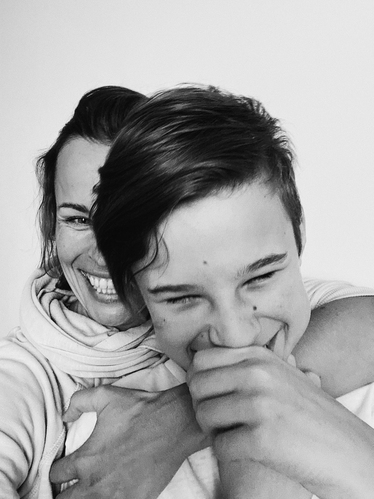 Svartvit bild av en mamma som kramar sin son bakifrån, båda skrattar.