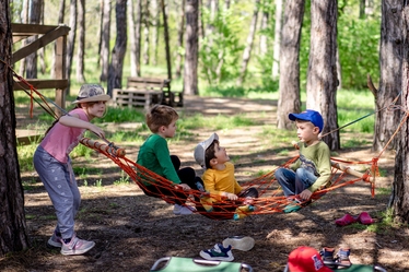 Fyra barn leker i en hängmatta i skogen.
