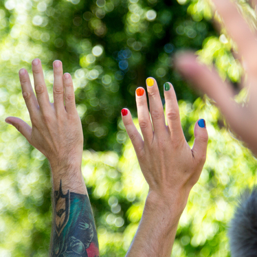 Händer sträcks upp i luften, några naglar är målade med pride-färger.