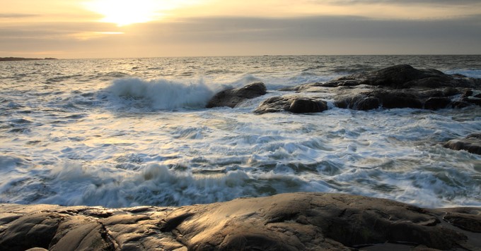 Solnedgång över havet med vågor som bryter mot klipporna.