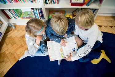 Tre barn framför bokhylla tittar i samma bok