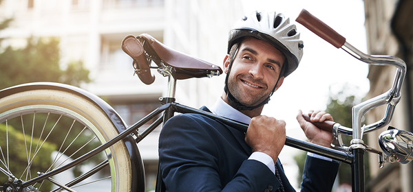 Tjänsteperson som bär på sin cykel, iklädd kostym och cykelhjälm. Foto: Yuri Arcurs / Mostphotos.com