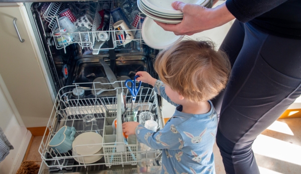 Ett barn hjälper sin förälder att plocka i diskmaskinen.