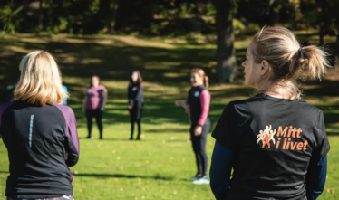 En grupp i träningskläder som står i ring.v deltagarna står vid tavla och skriver.