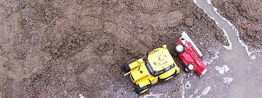 En gul och en röd leksaksbil i sandlåda med vatten i diken