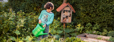 Barn i pyjamas som vattnar plantering med vattenkanna