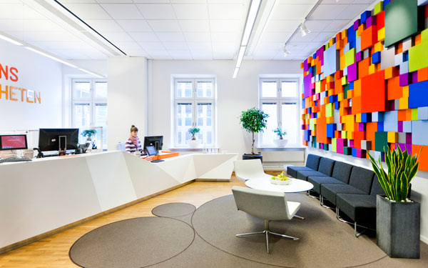 Modernt kontorslandskap med färgglad vägg och avslappnad sittgrupp.