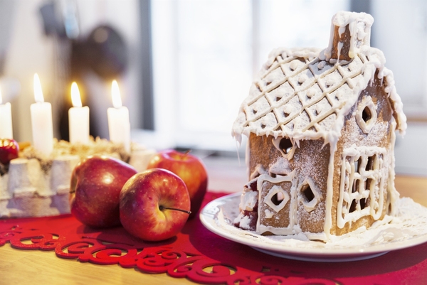 Hemgjord pepparkakshus på ett bord, omgiven av röda äpplen och brinnande ljus.