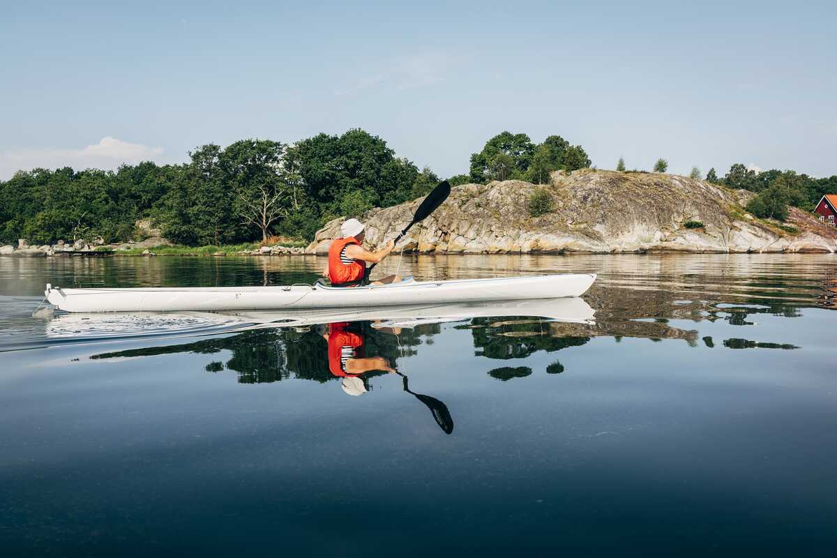 Person som paddlar kajak i lugnt vatten nära klippor och skog.