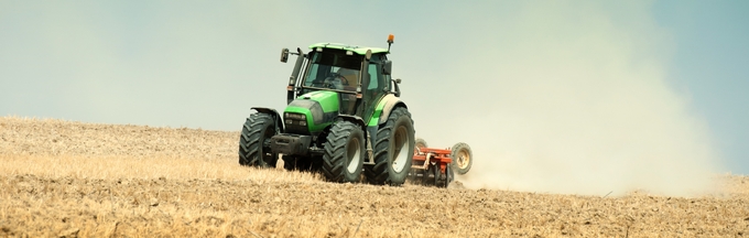 Grön traktor kör på ett torrt fält mot en klar himmel.