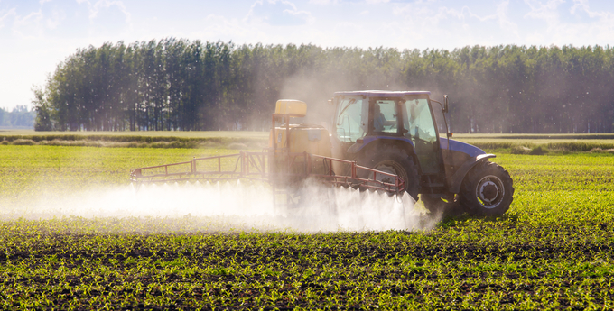 Traktor som sprider bekämpningsmedel på ett grönt fält i solsken.