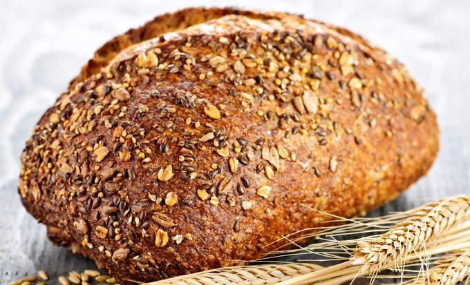 Närbild på ett rustikt bröd täckt med frön, bredvid vetekärvar.
