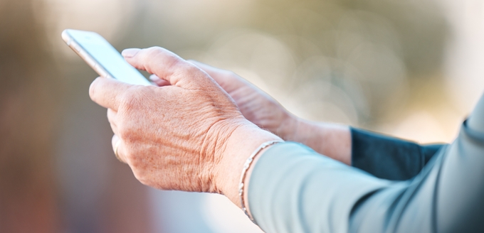 Äldre person använder en smartphone utomhus.