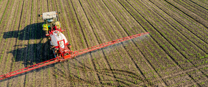 Luftvy av en traktor som sprider växtskyddsmedel på ett grönt fält.