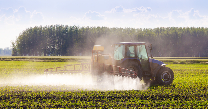 Traktor som besprutar åkermark med grön gröda