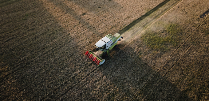 Skördetröska som skördar ett åkerfält, sedd uppifrån.