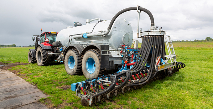 Traktor med flytgödseltank och spridningsslangar på en grön åker