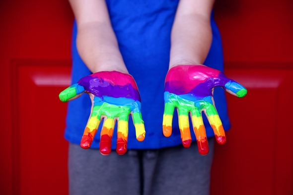 Barnhänder med fingerfärg på i alla regnbågens färger.