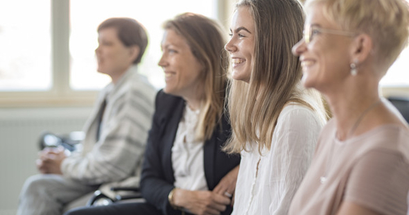 Fyra personer sittande i rad, skrattar och ser åt vänster.