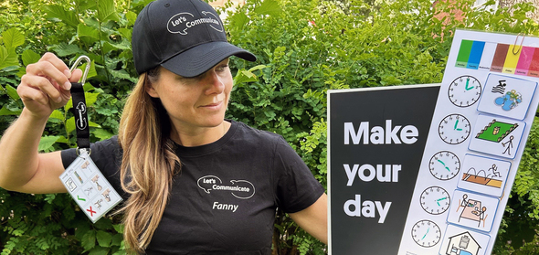 Fanny från Infoteket har keps med texten Let´s Communicate. Hon håller i nyckelband med samma text. Håller skylt med texten "Make your day" och bildsymboler.