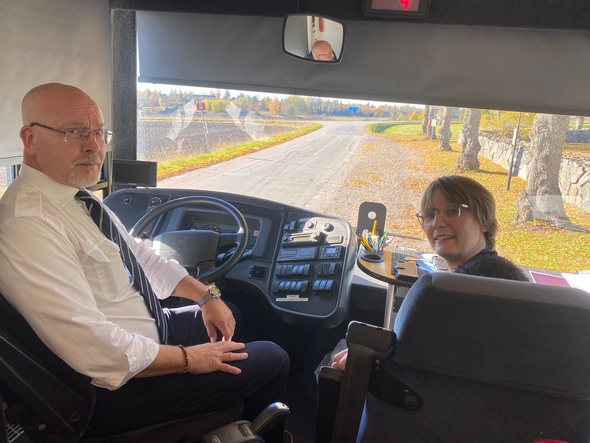 Busschauffören och bibliotekarien sitter framme i bussen, med vägen framför synlig genom bussrutan.