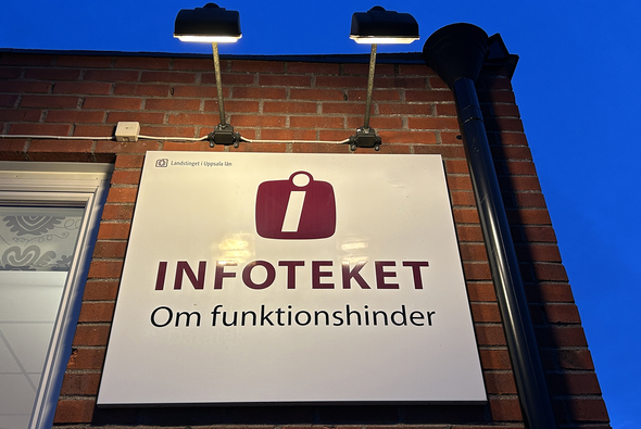 Skylt för "Infoteket om funktionshinder" upplyst av lampor på en tegelväggsfasad.