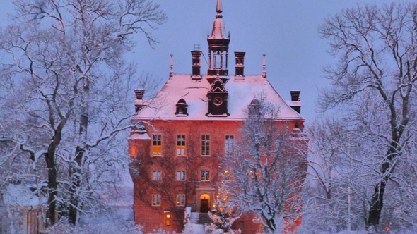 Rött slott omgivet av snötäckta träd i skymningen.