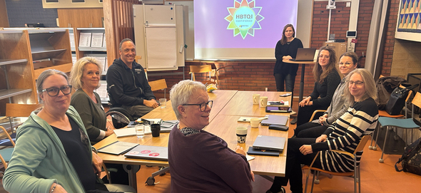 Grupp av personer som deltar i ett möte med en presentation i bakgrunden.