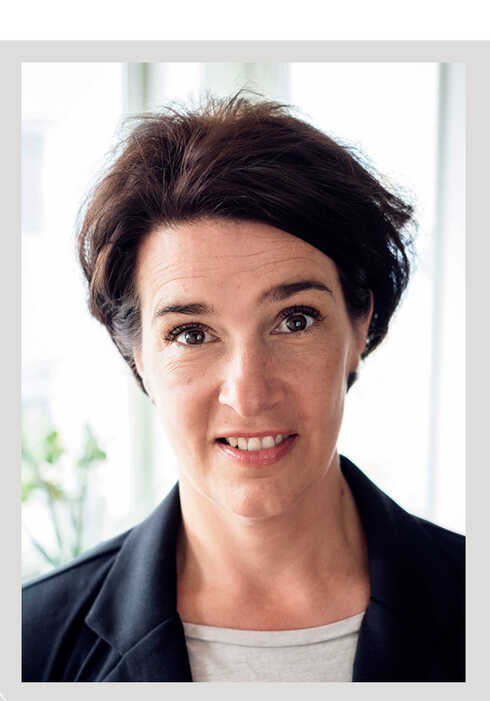 Närbild av en leende kvinna med mörk kavaj och grå tröja.