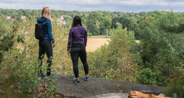 Två kvinnor betraktar landskapet från en skogsbevuxen utsiktspunkt.