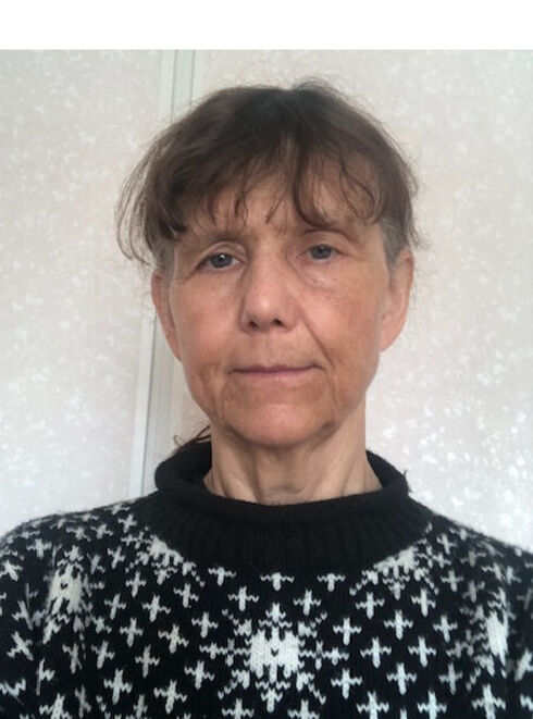 Person i svart- och vitmönstrad tröja står mot en tapetserad vägg.