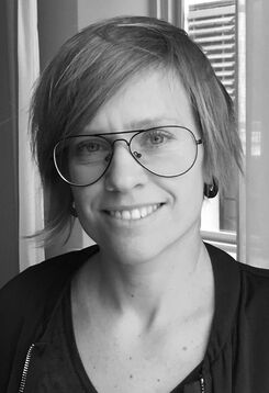 Svartvit porträtt av en leende person med glasögon.