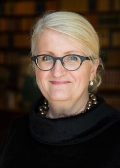 Porträttbild av leende kvinna med ljust hår och glasögon.