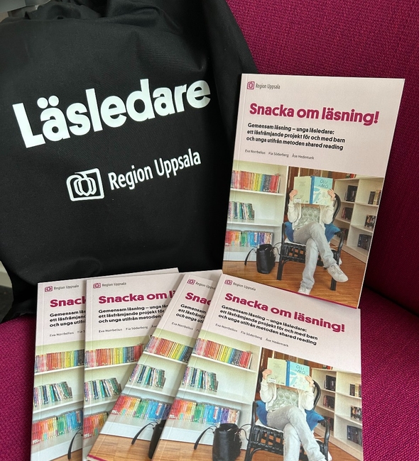 Tryckta rapporter med titeln Snacka om läsning, med en person på omslaget som sitter i en stol och håller i en barnbok framför ansiktet. En svart tygkasse bredvid, med texten Läsledare Region Uppsala