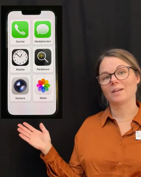 Kvinna i orange skjorta som presenterar en stor modell av en mobiltelefon med basapplikationer.