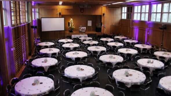 Inredd festlokal med runda bord och juldekorationer.