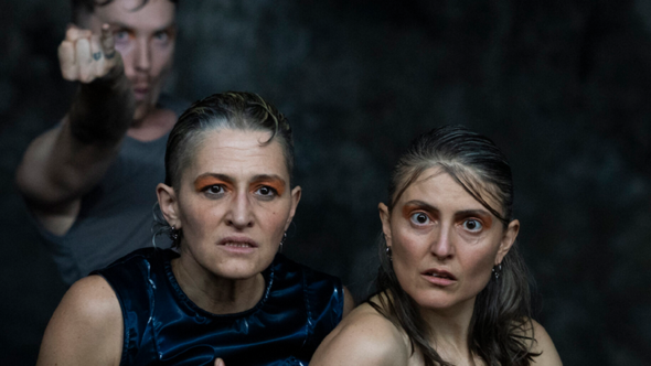 Tre personer med intensiva blickar; två kvinnor i förgrunden ser chockade medan en person i bakgrunden pekar.