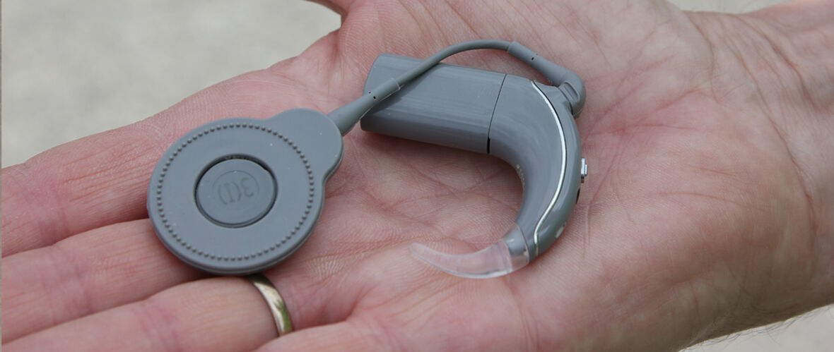 Grå processor och magnet för cochleaimplantat - liknar hörapparat som ligger i en öppen handflata.