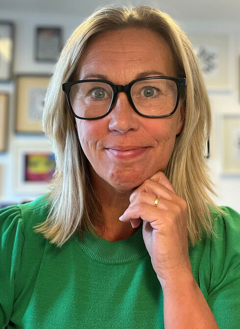 Porträtt av leende kvinna med glasögon och grön tröja.