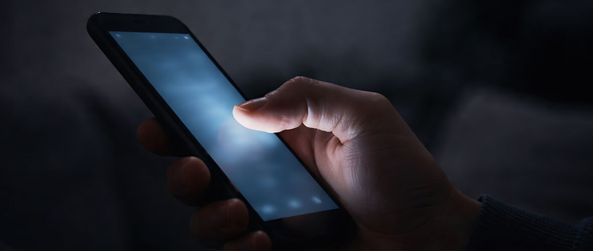 Hand som använder en mobiltelefon i mörker.