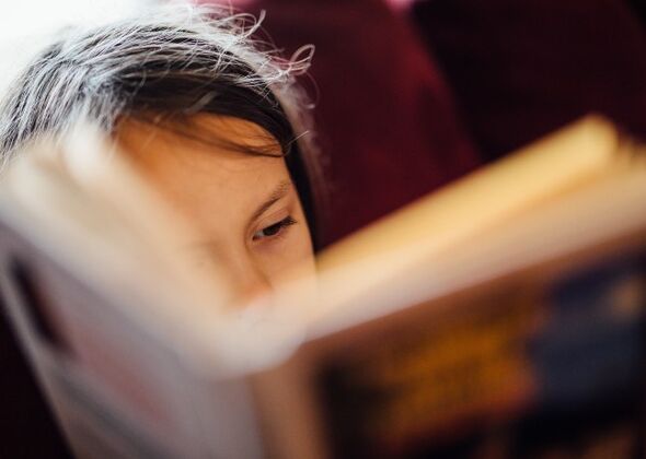 Ett ansikte skymtar fram bakom en bok.