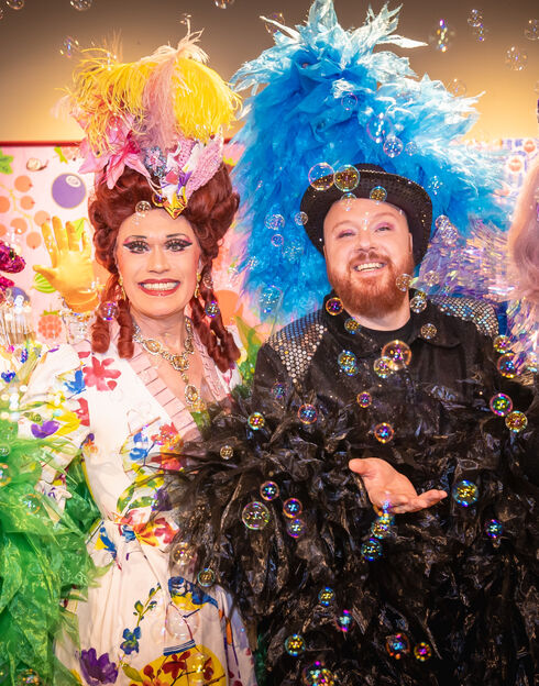 Två leende artister i färgglada fjäderdräkter omgivna av flytande bubblor