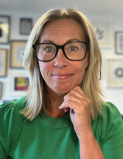 Porträtt av leende kvinna med glasögon och grön tröja.