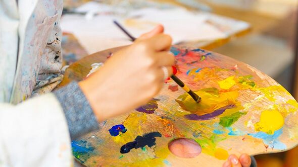 Närbild på en hand som blandar färger på en målarpalett