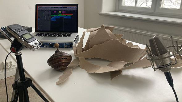 Hemmastudio på skrivbord med mikrofon, bärbar dator, ljudinspelare, en träsnurra och rivet papp.
