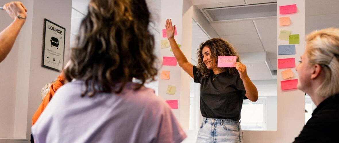 Person håller upp en post-it och leder en gruppdiskussion i ett kreativt möte.