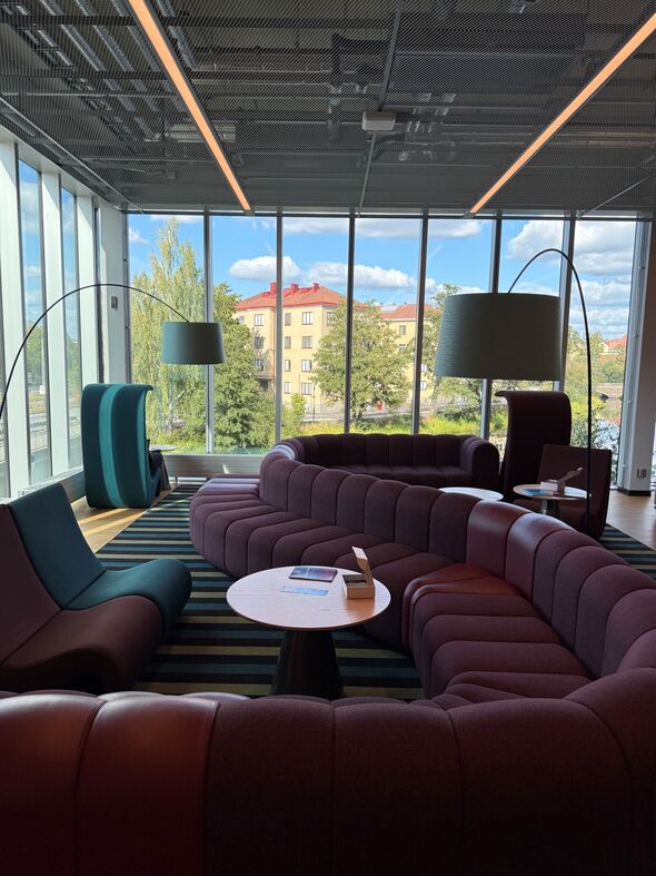 En vinröd ringlande lång soffa, stora golvlampor som böjer sig in över soffan och stora fönster runt om.