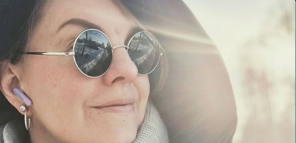 Person i huva och runda solglasögon med litet lila headset och solglimt i bakgrunden